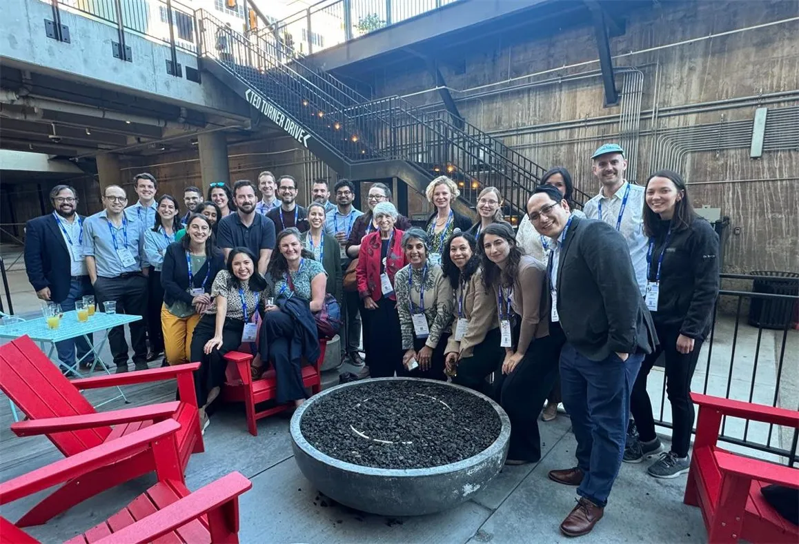 Around thirty members of the group gathered around a fire pit at a conference reception, wearing conference lanyards.